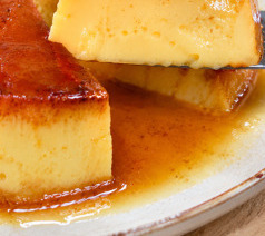 Unmolded condensed milk flan on a white plate with golden caramel sauce pooling around it